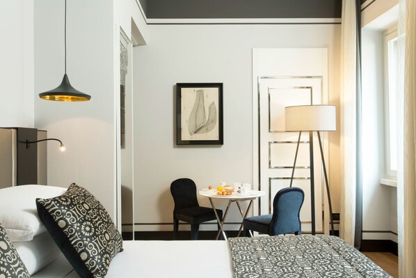 Een hotelkamer met een bed, twee stoelen, een tafel met ontbijt, een lamp en een lijst met een kunstwerk aan de muur.