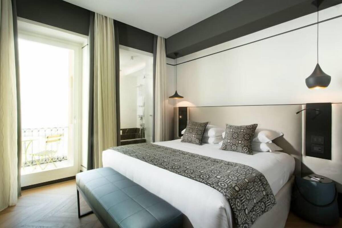 Une chambre d’hôtel moderne avec un grand lit, des lampes de chevet et une vue sur un balcon.
