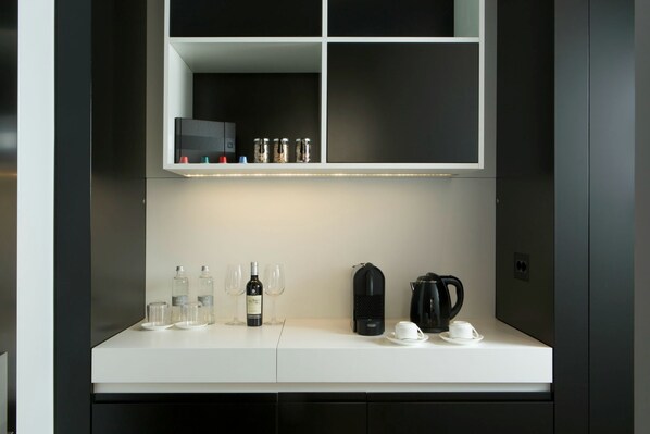 Een moderne keuken met een wit aanrecht, wijnflessen, glazen, een koffiezetapparaat en een waterkoker.