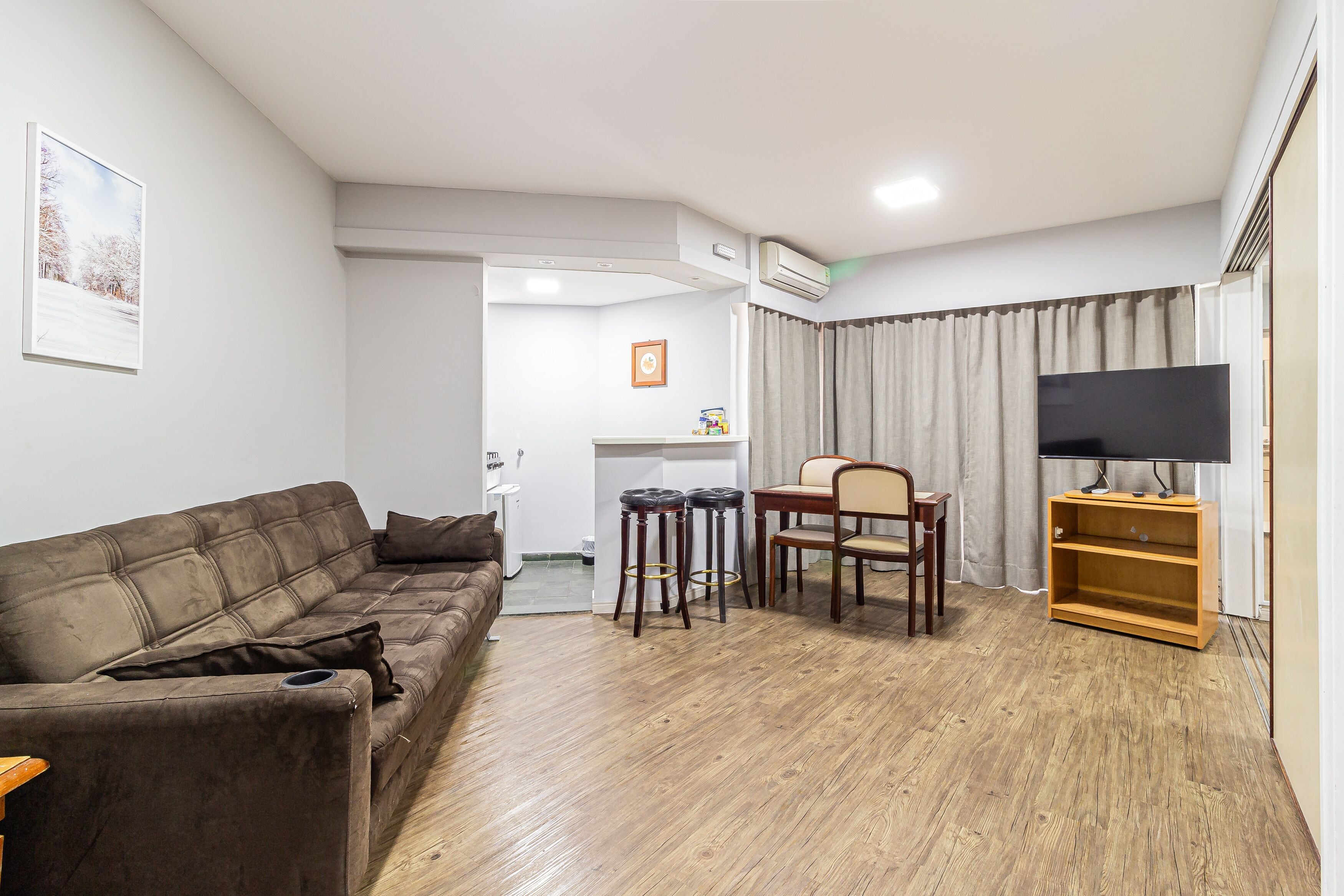 A living room with a brown sofa, a wooden TV stand, and a dining area with a table and chairs.