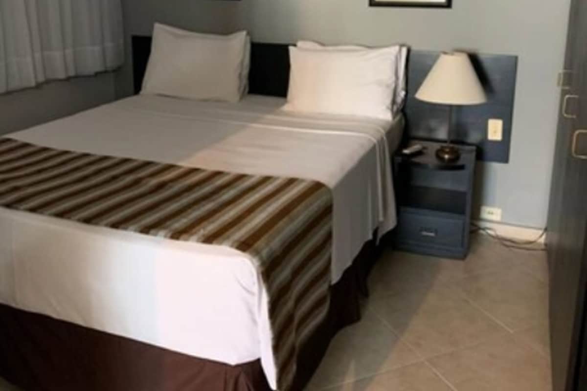 Una camera d'albergo con un letto, un condizionatore, un comodino, una lampada e un quadro appeso al muro.