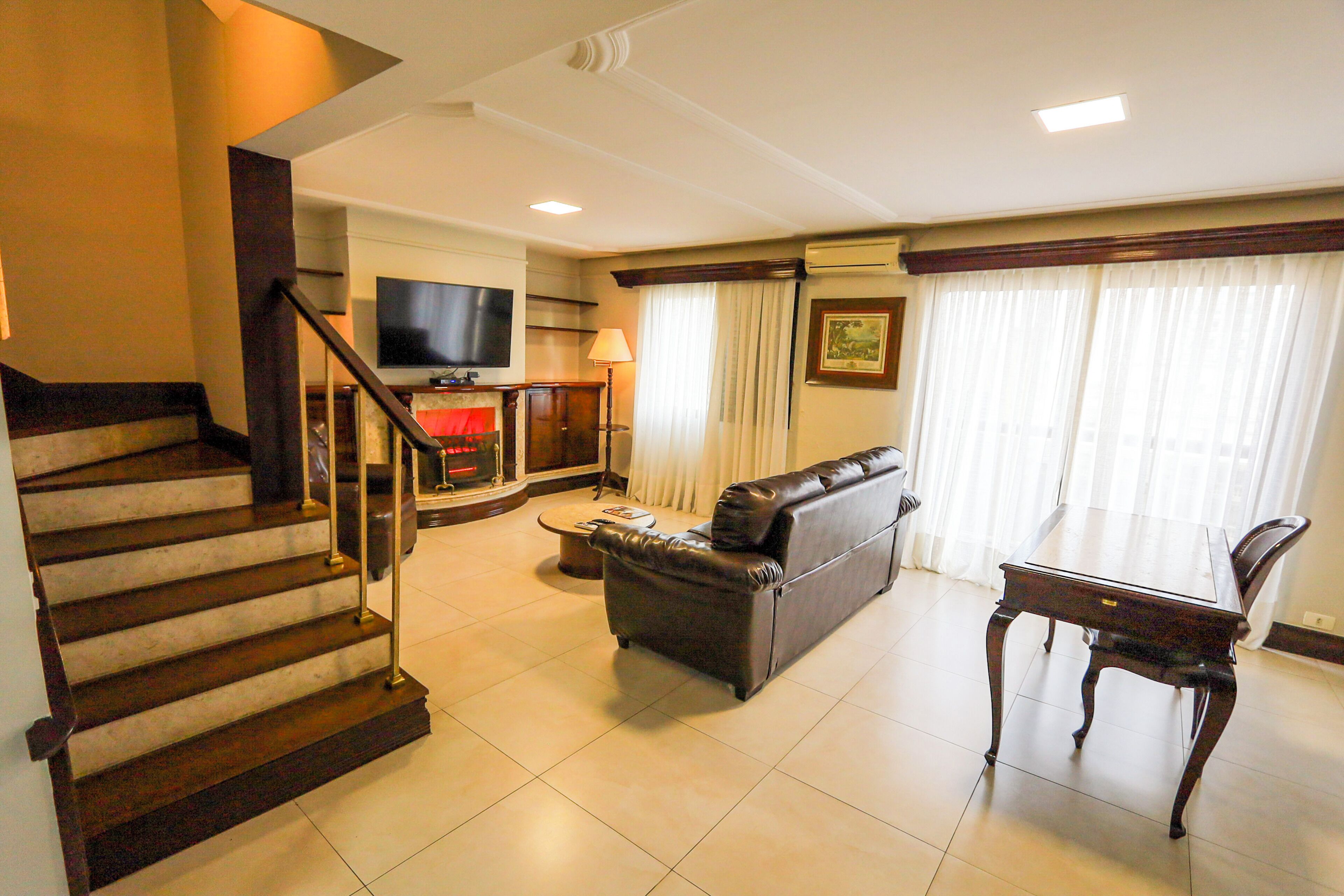 A living room with a sofa, a television, a fireplace, a dining table, and a staircase.