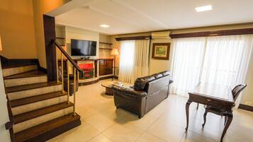 A living room with a sofa, a television, a fireplace, a dining table, and a staircase.