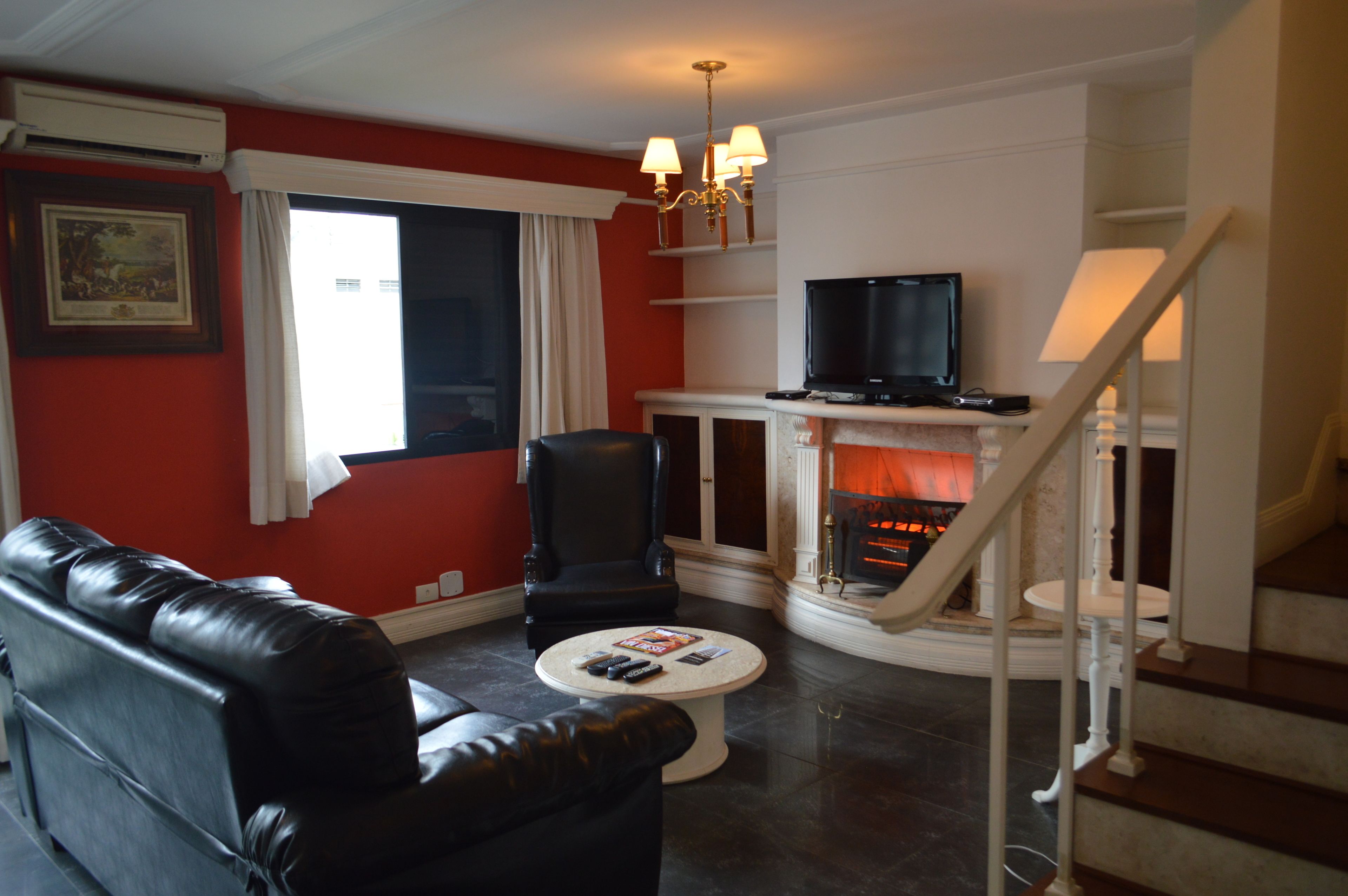 A living room with a black leather sofa, a round coffee table with remotes, a fireplace, and a TV on a stand.