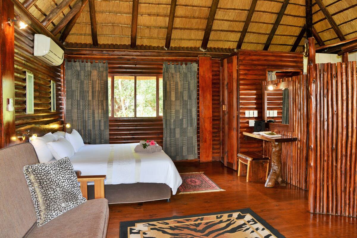 A log cabin bedroom with a bed, a sofa, a small table, and a chair.