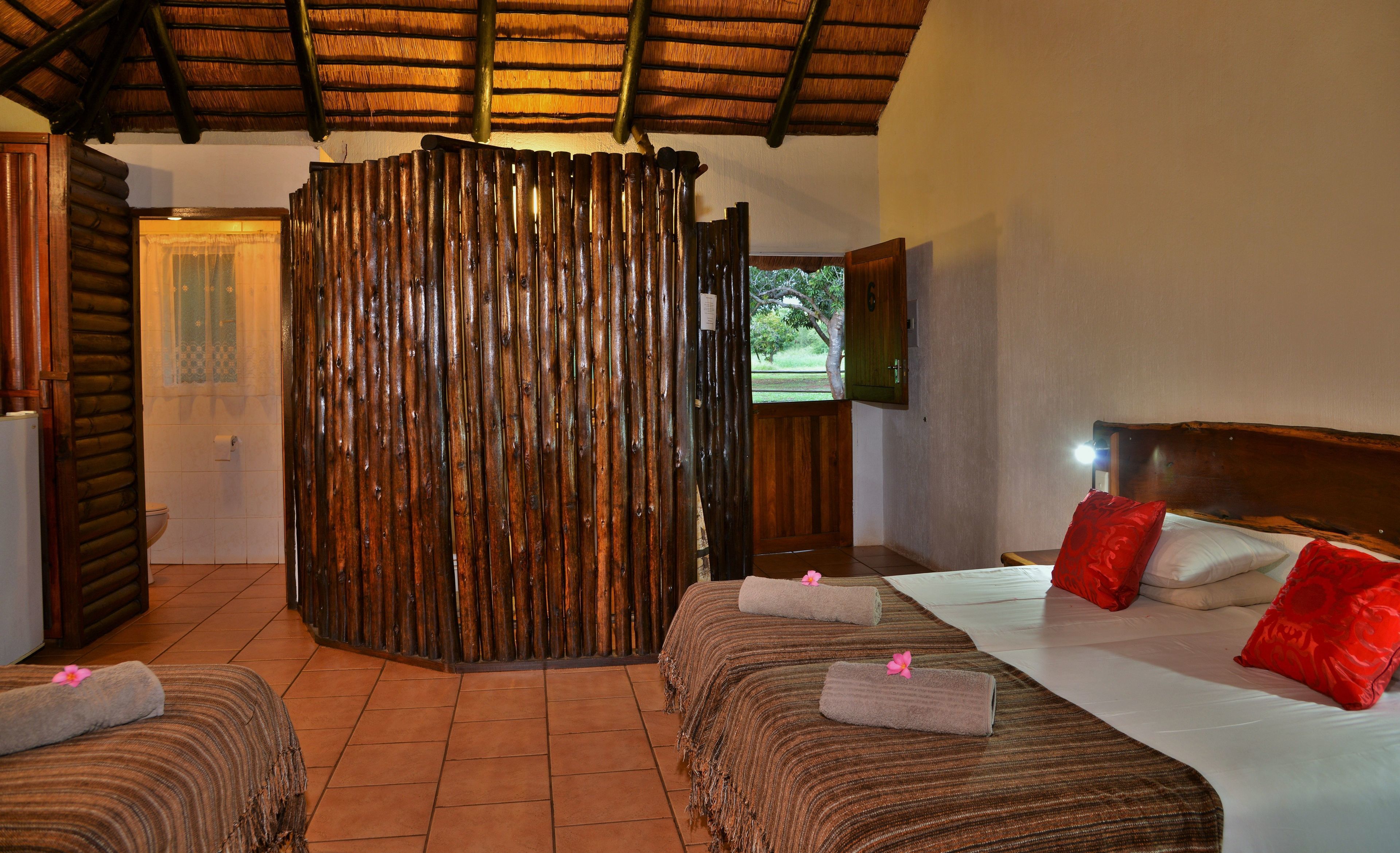 A room with a bed, two bedside tables, a wooden partition, and a view of the outdoors.