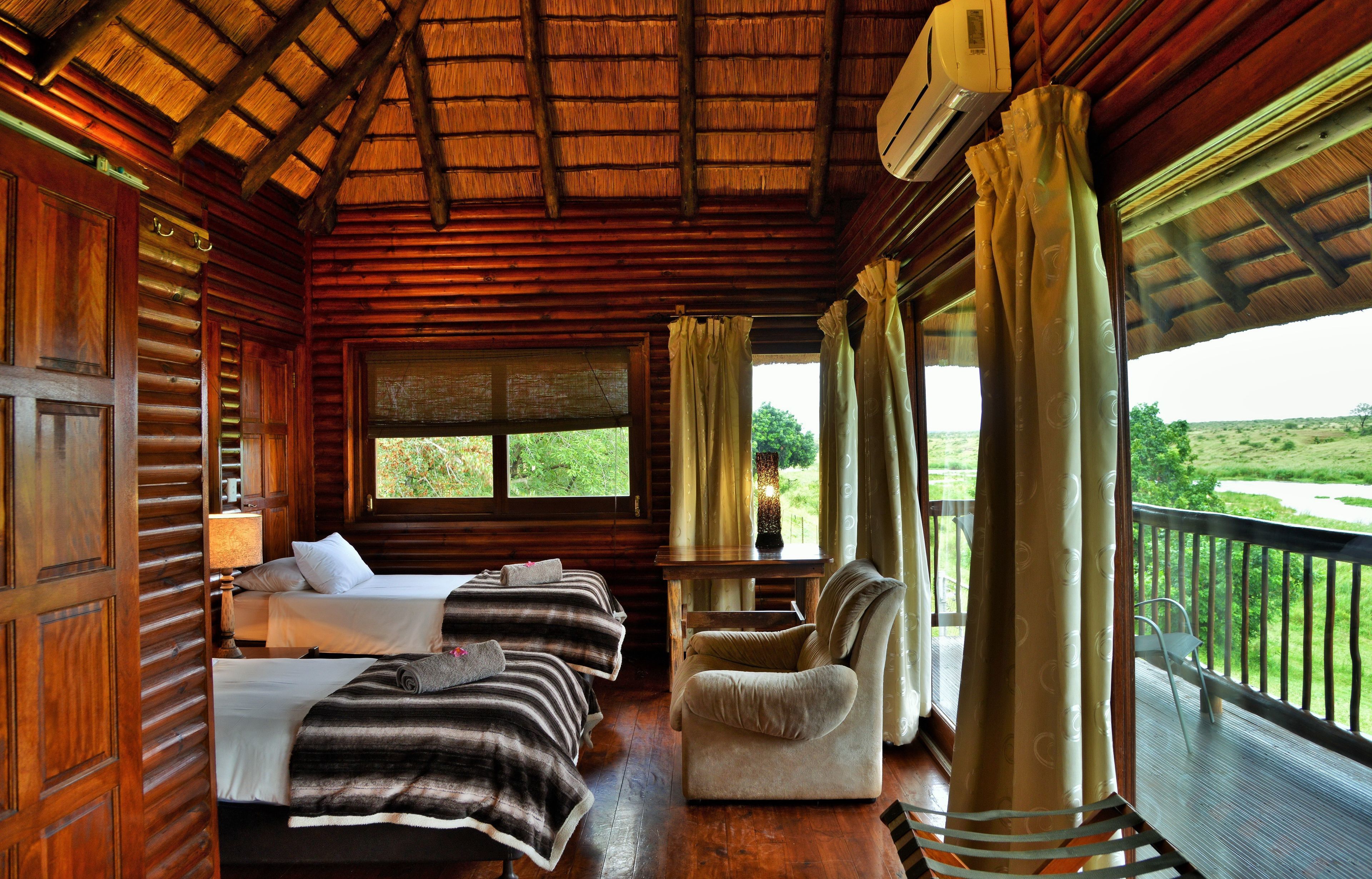 A wooden cabin with two beds, a sofa, a table, and a balcony with a view of the landscape.