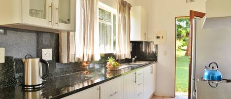 Una cocina con armarios blancos, encimera negra, una tetera y un frutero.