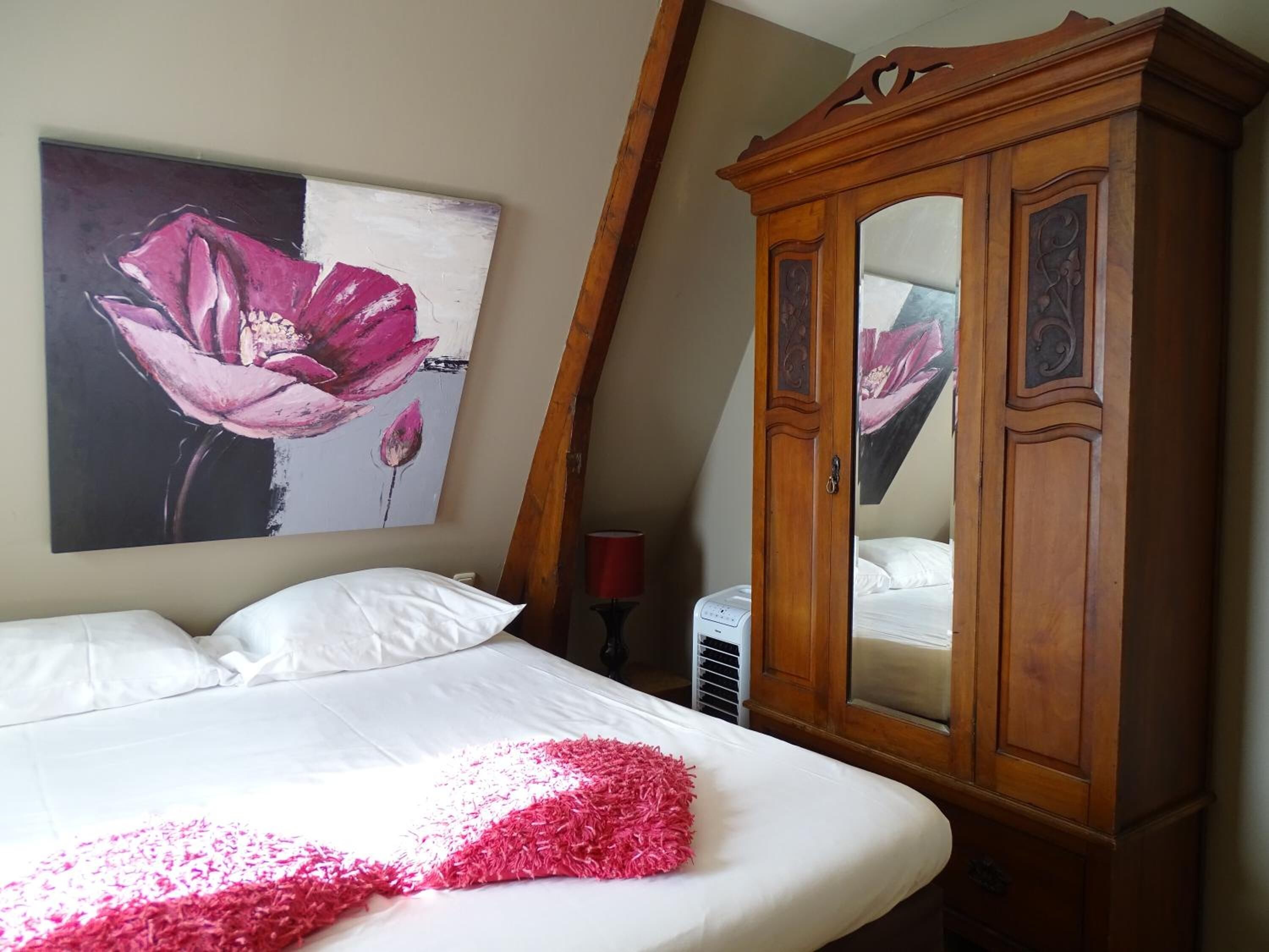A bedroom with a bed, a wooden wardrobe, a wall-mounted painting of a flower, and a radiator.