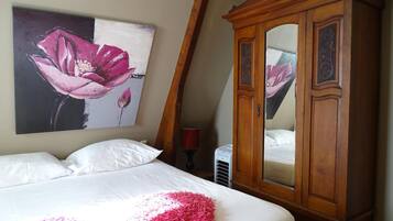 A bedroom with a bed, a wooden wardrobe, a wall-mounted painting of a flower, and a radiator.