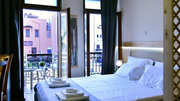 Une chambre d’hôtel avec un lit, une table et une vue sur la ville par de grandes fenêtres ouvertes.