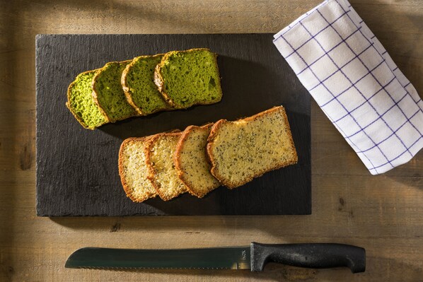 Rebanadas de pan verde y de grano entero sobre una tabla de pizarra con un cuchillo y un mantel a cuadros.