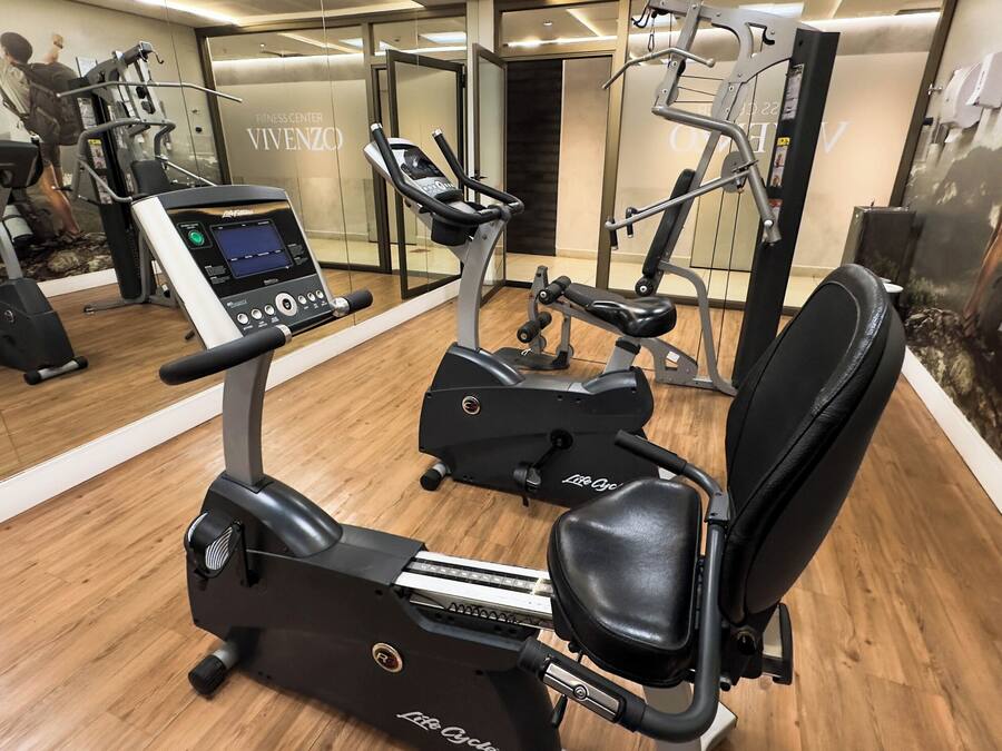 A fitness center with cardio machines, including an elliptical and a stationary bike, and a mirrored wall.