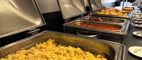 A buffet with various food items including scrambled eggs, a red sauce, and other dishes.