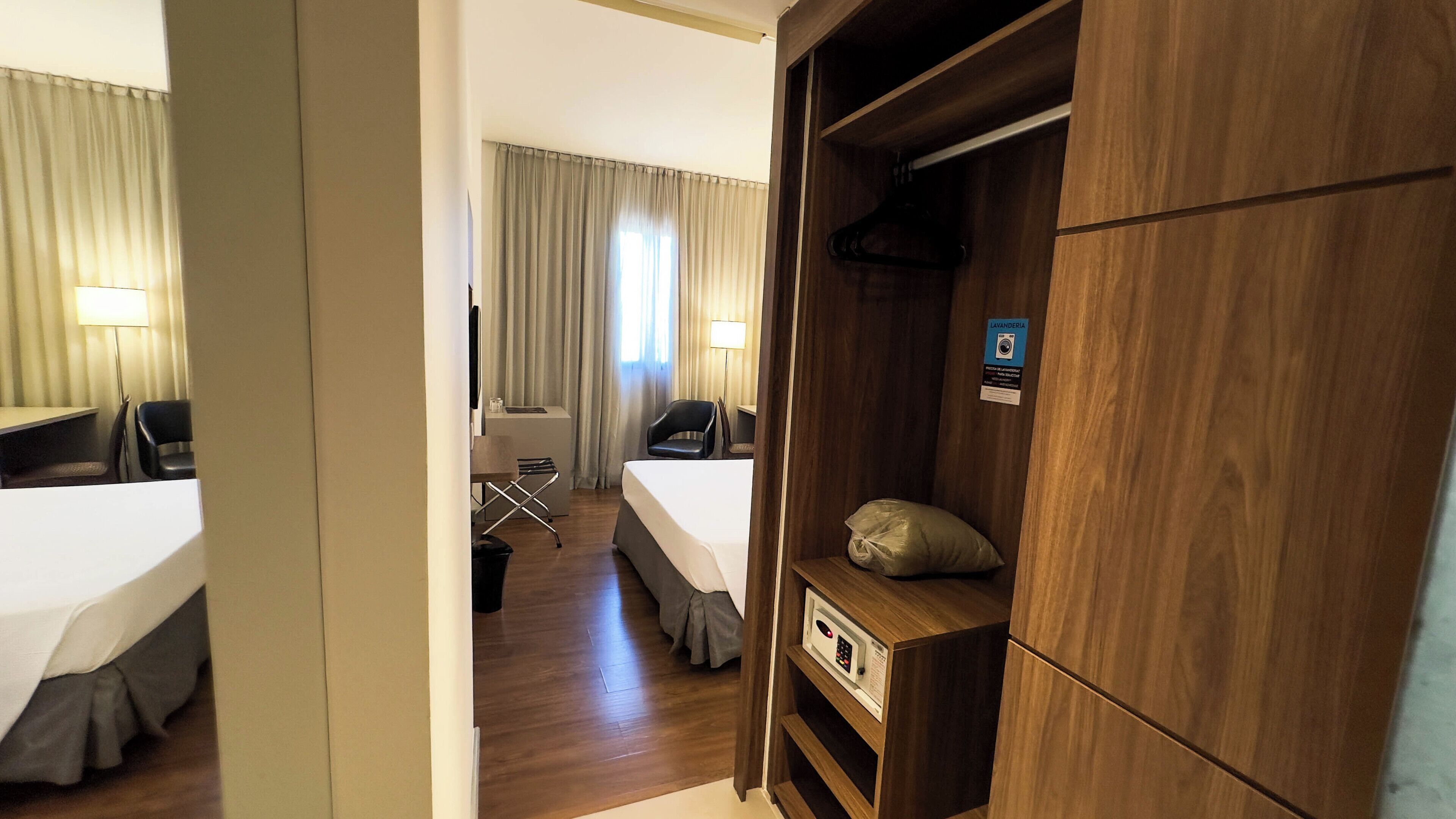 A hotel room with a bed, a desk, a chair, a wardrobe, and a mirror.