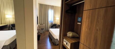 Una habitación de hotel con cama, escritorio, silla, armario y espejo.