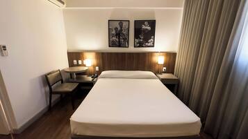 A hotel room with a bed, a desk, a chair, two bedside lamps, and two framed pictures on the wall.