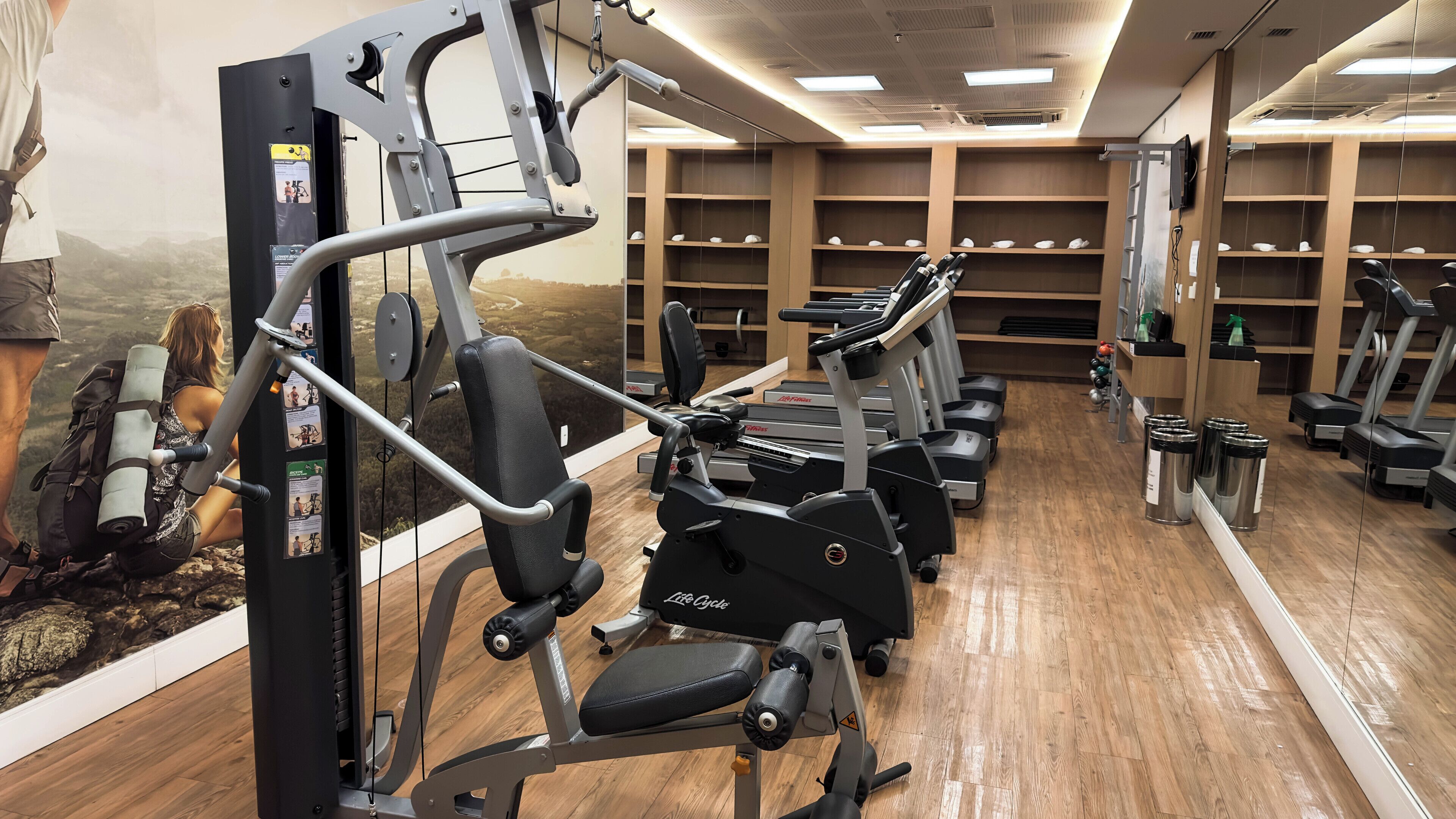 A gym with cardio machines, weight stations, and a mirrored wall.