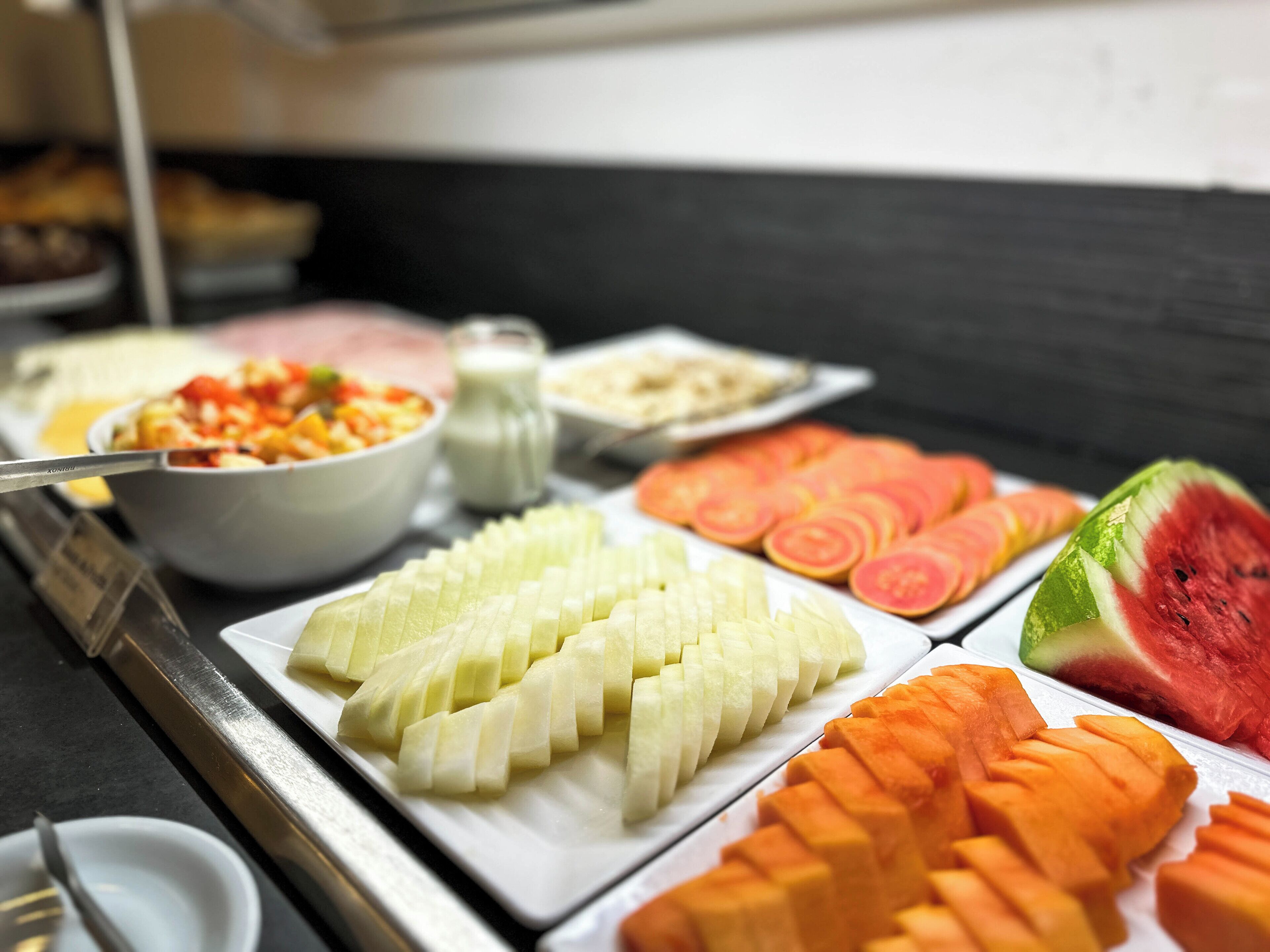 A buffet with various sliced fruits and vegetables, including watermelon, cantaloupe, and carrots.