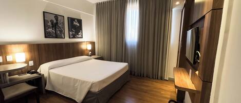Una habitación de hotel con cama, mesita de noche, lámpara y televisor.