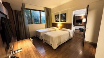 A hotel room with two beds, a desk, a TV, and a window with curtains.
