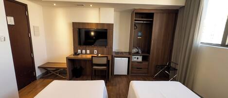 Habitación de hotel con dos camas, un escritorio con computadora, televisor, refrigerador pequeño y armario.