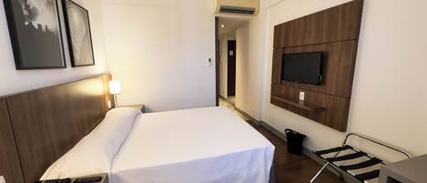 A hotel room with a bed, a TV mounted on the wall, a desk, and a chair.