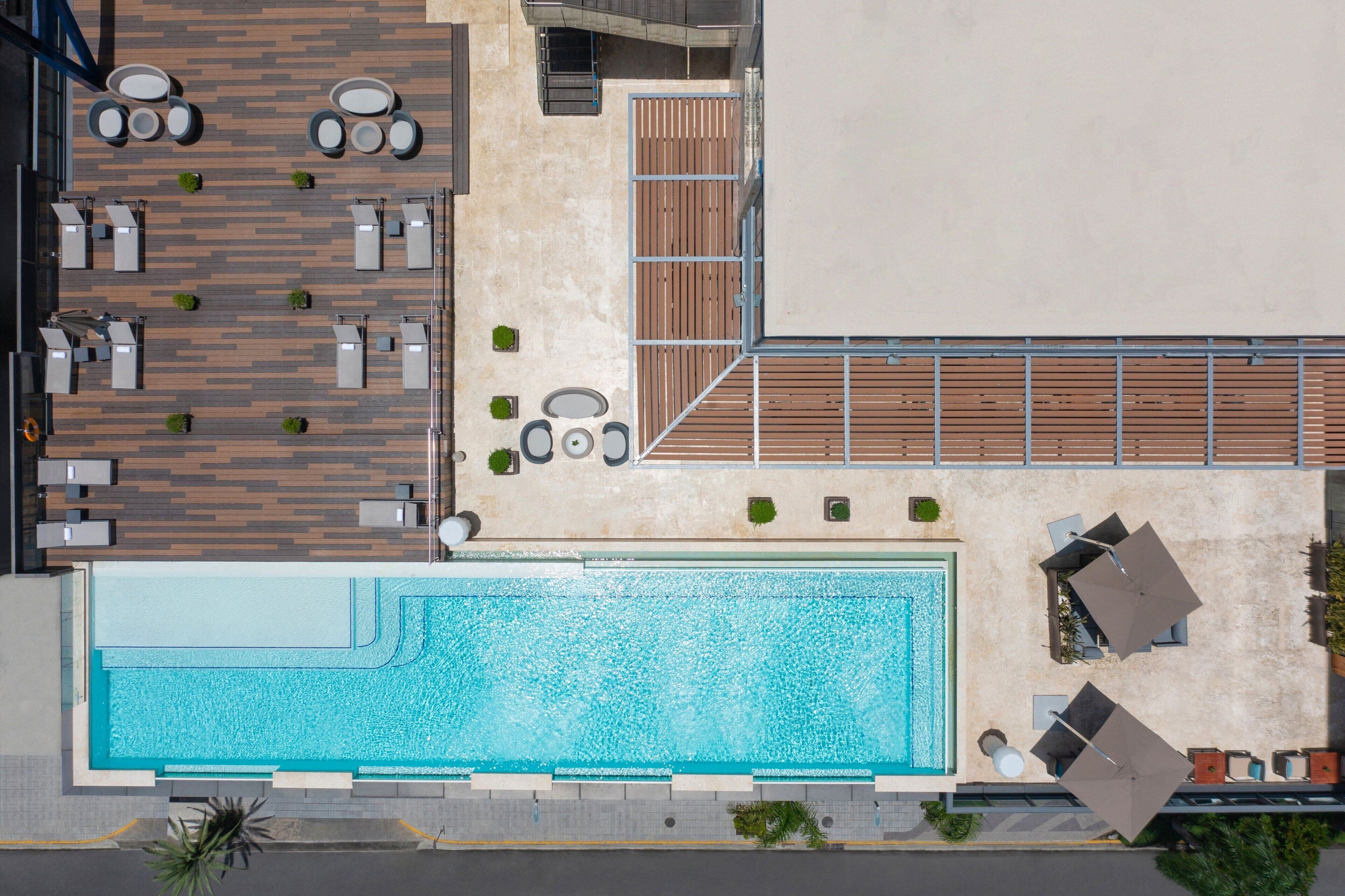 Vue aérienne d’un hôtel doté d’une grande piscine, d’espaces de détente en plein air et d’une terrasse en bois.