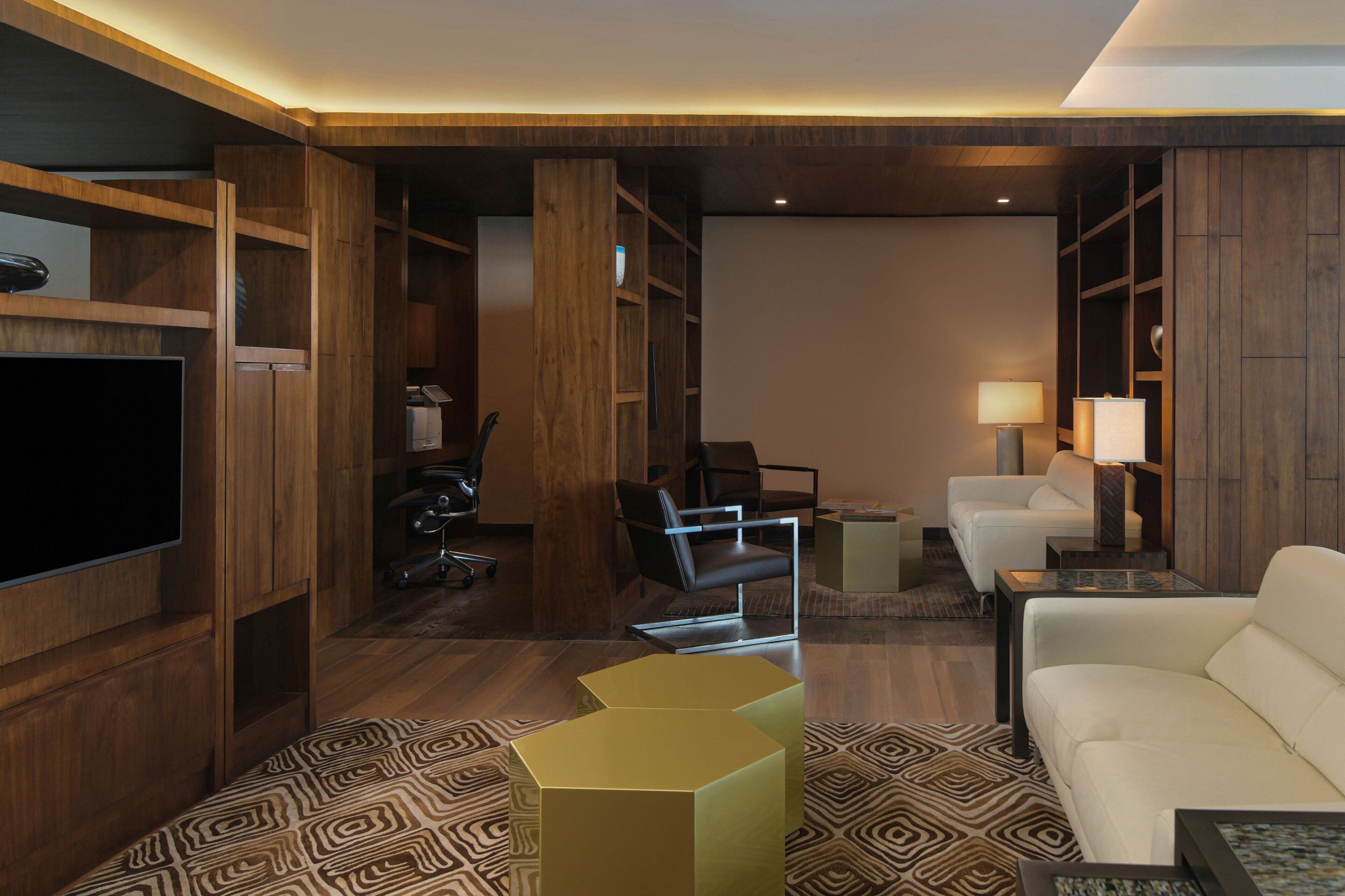 A modern hotel room with a large flat-screen TV, a sofa, a dining table, and a lamp.