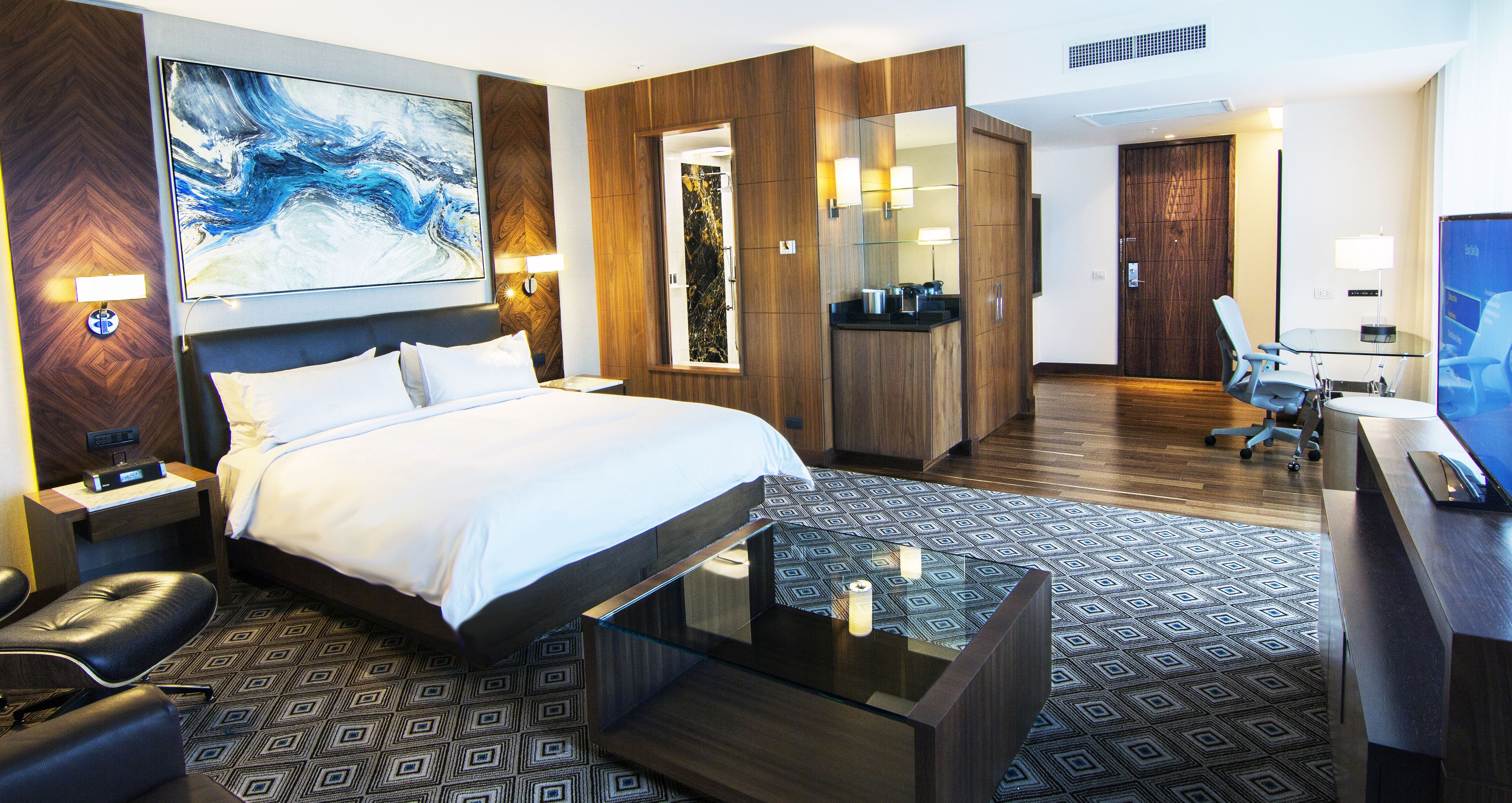 Hotelkamer met een groot bed, een bureau, een stoel, een televisie en een badkamer met spiegel en wastafel.