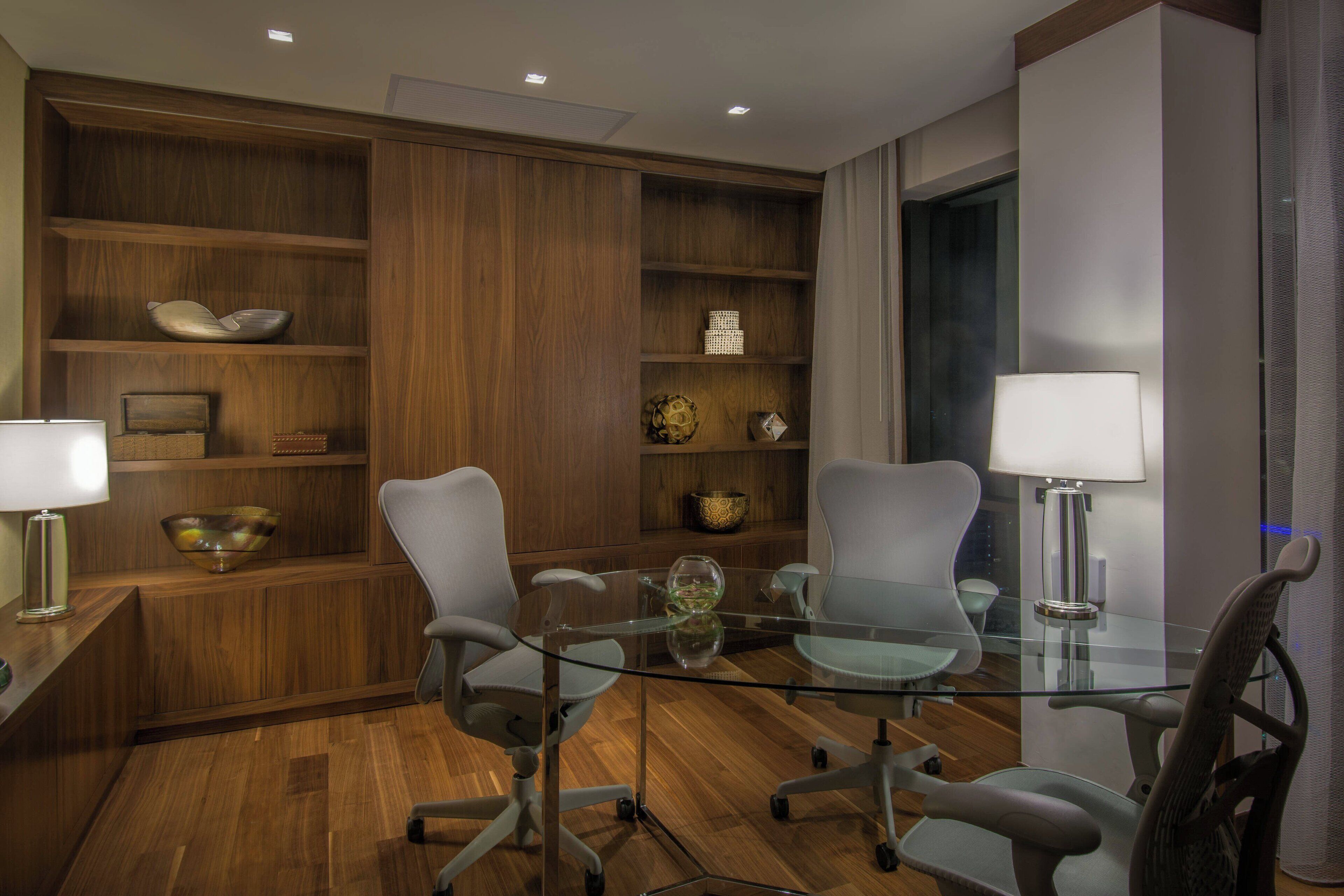 A modern meeting room with glass tables, office chairs, wooden shelving, and lamps.