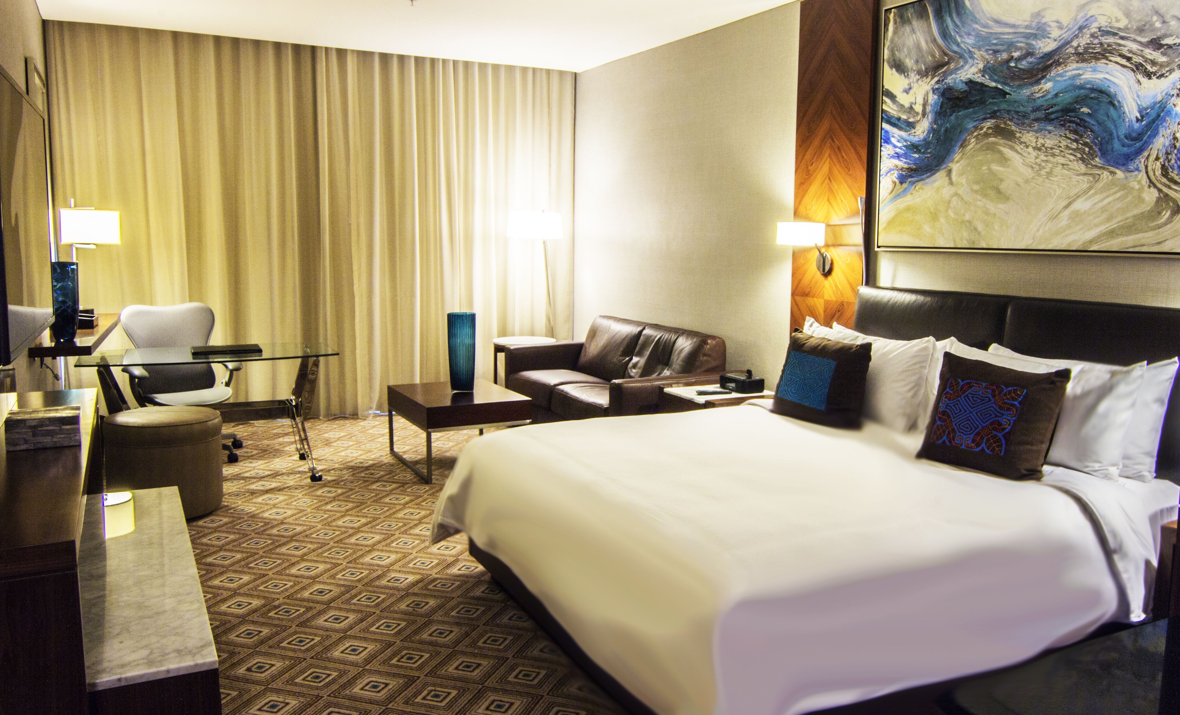 Une chambre d’hôtel avec un grand lit, un canapé en cuir, une table basse en verre, un bureau et une chaise.