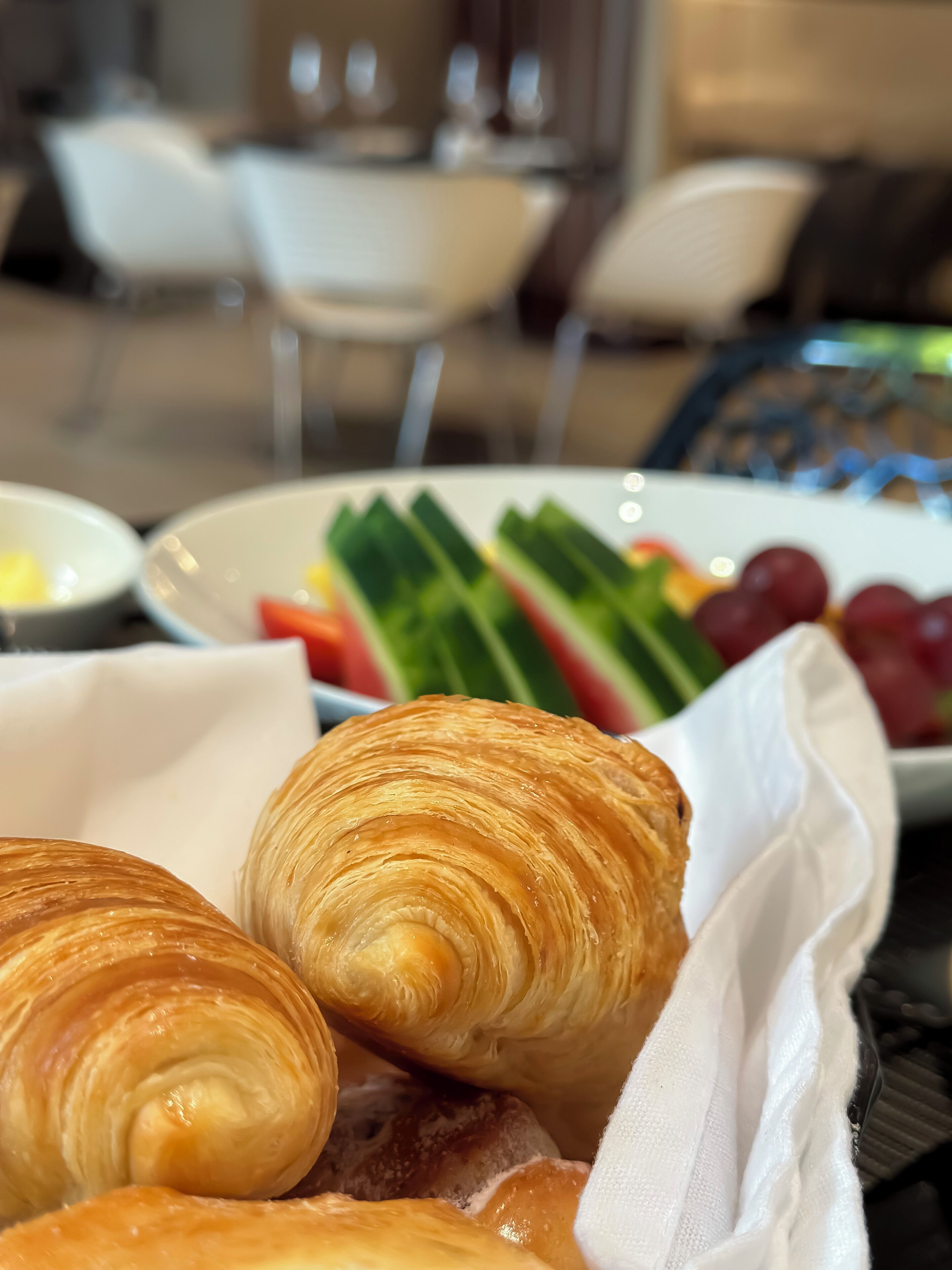 A table with croissants, a plate of fruits, and a white napkin.