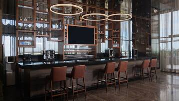 Zona de bar moderna con una gran pantalla de televisión, varios estantes con botellas y taburetes.