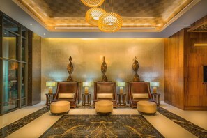 A lobby with four armchairs, a central ottoman, and three lamps on side tables.