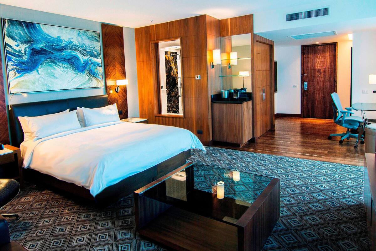 Habitación de hotel con una cama grande, un escritorio, una silla, un armario y un baño con espejo y lavabo.