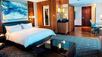 A hotel room with a large bed, a desk, a chair, a wardrobe, and a bathroom with a mirror and sink.