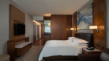 Quarto de hotel com uma cama grande, uma televisão presa na parede, uma mesa com abajur e um quadro sobre a cama.