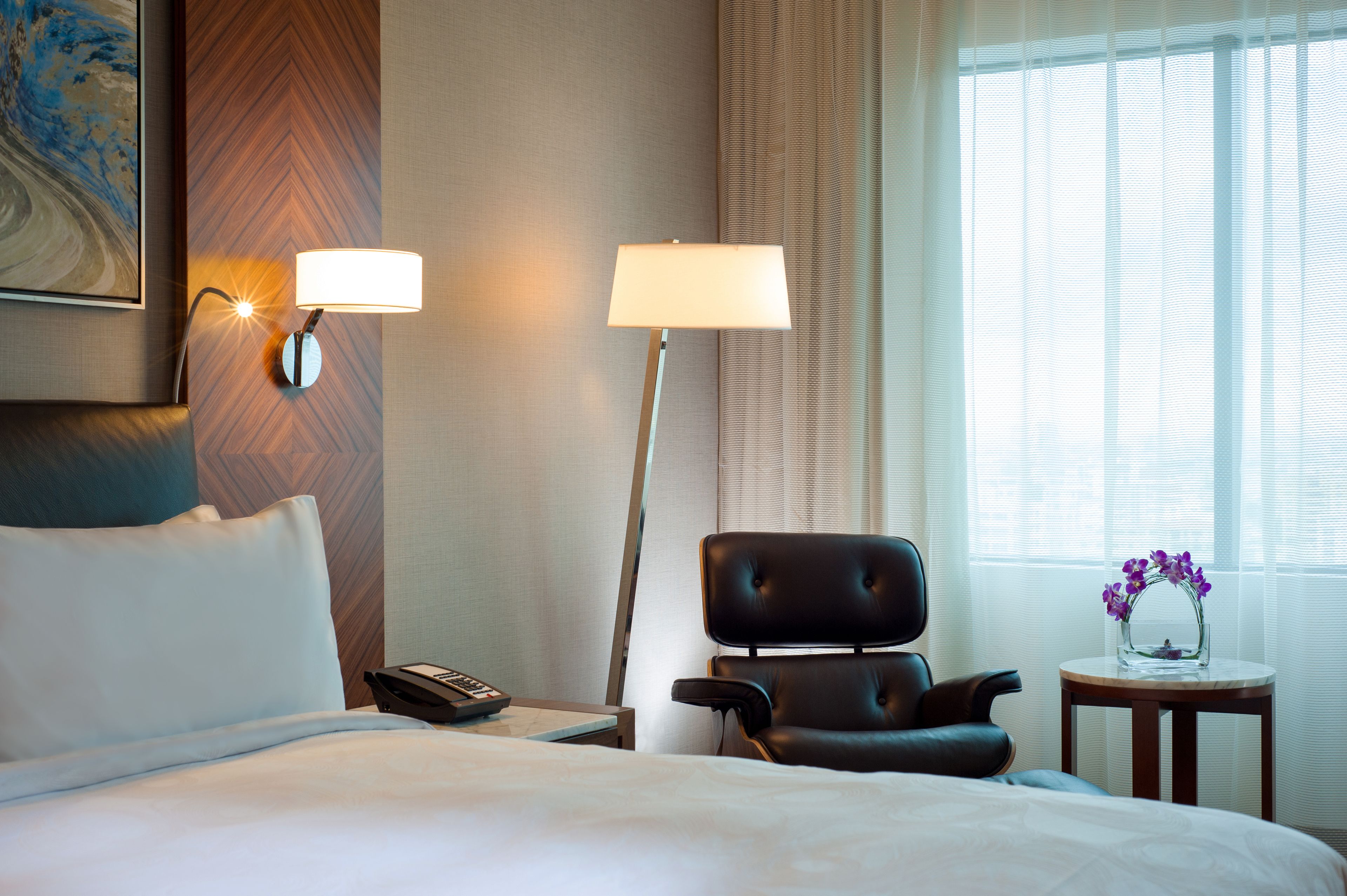 Une chambre d’hôtel avec un lit, un bureau avec un téléphone, une chaise, une lampe et un vase avec des fleurs.