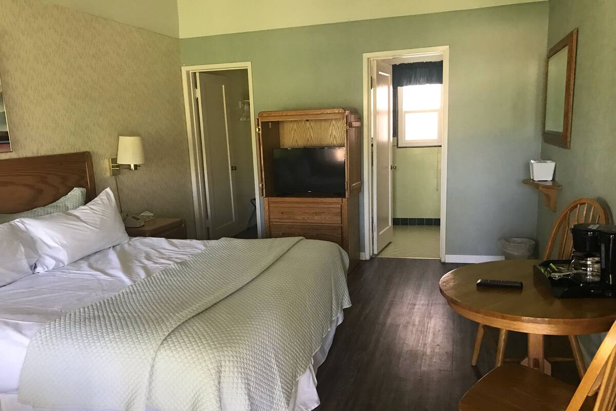 A hotel room with a bed, a TV, a coffee maker, and a chair.