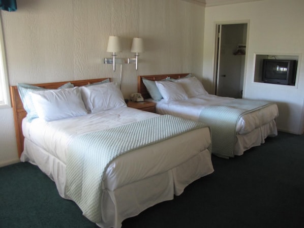 A hotel room with two beds, each with white linens and a wooden headboard. There are two wall-mounted lamps on the wall above the beds. - Bridge Bay Lodge at Shasta Lake (Redding)