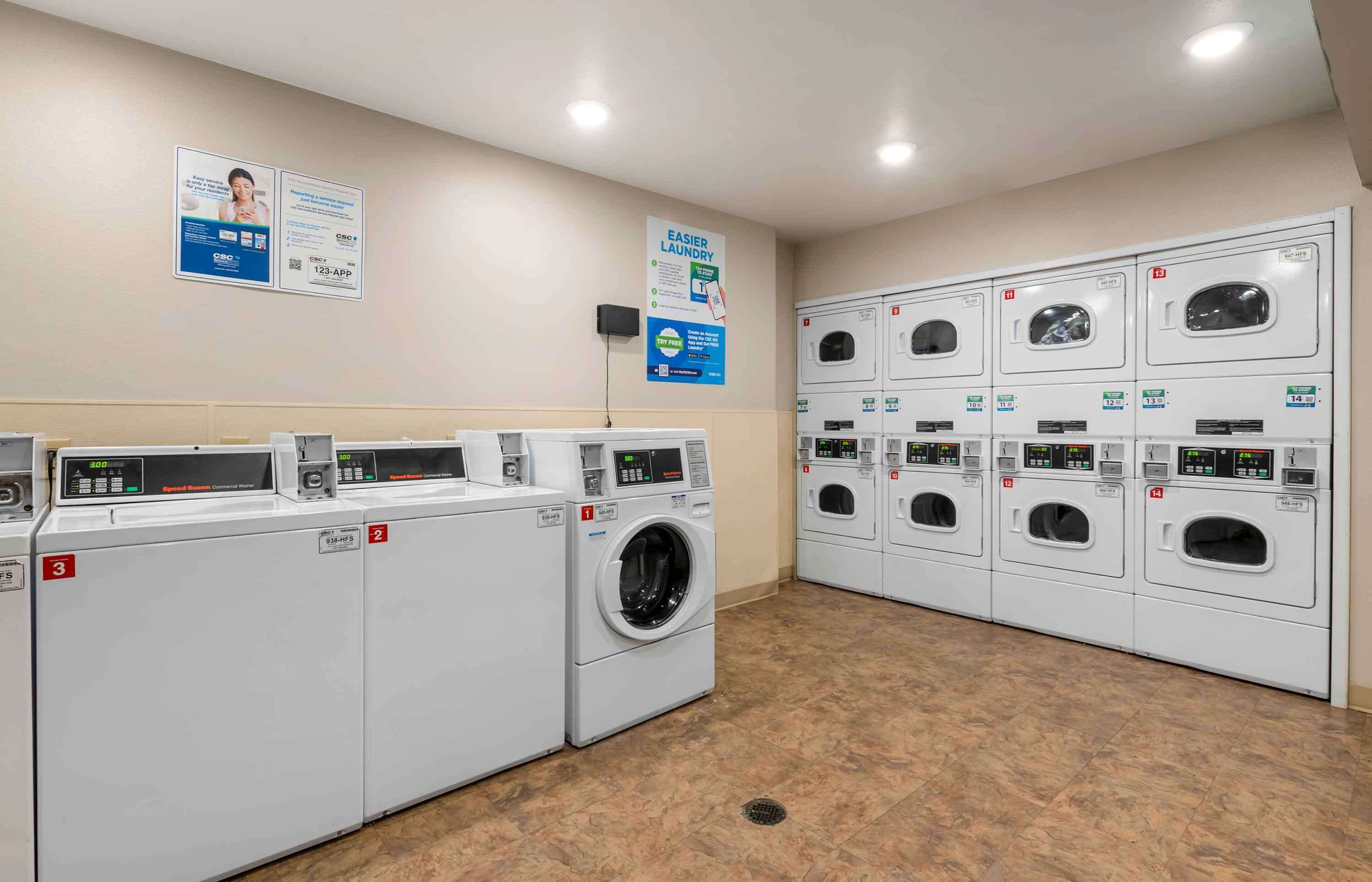 A laundromat with multiple washing machines and dryers, numbered from 1 to 14, and a sign promoting a 123-App.
