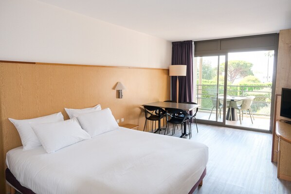Une chambre d’hôtel avec un grand lit, un bureau avec des chaises, une télévision et un balcon équipé d’une table et de chaises.