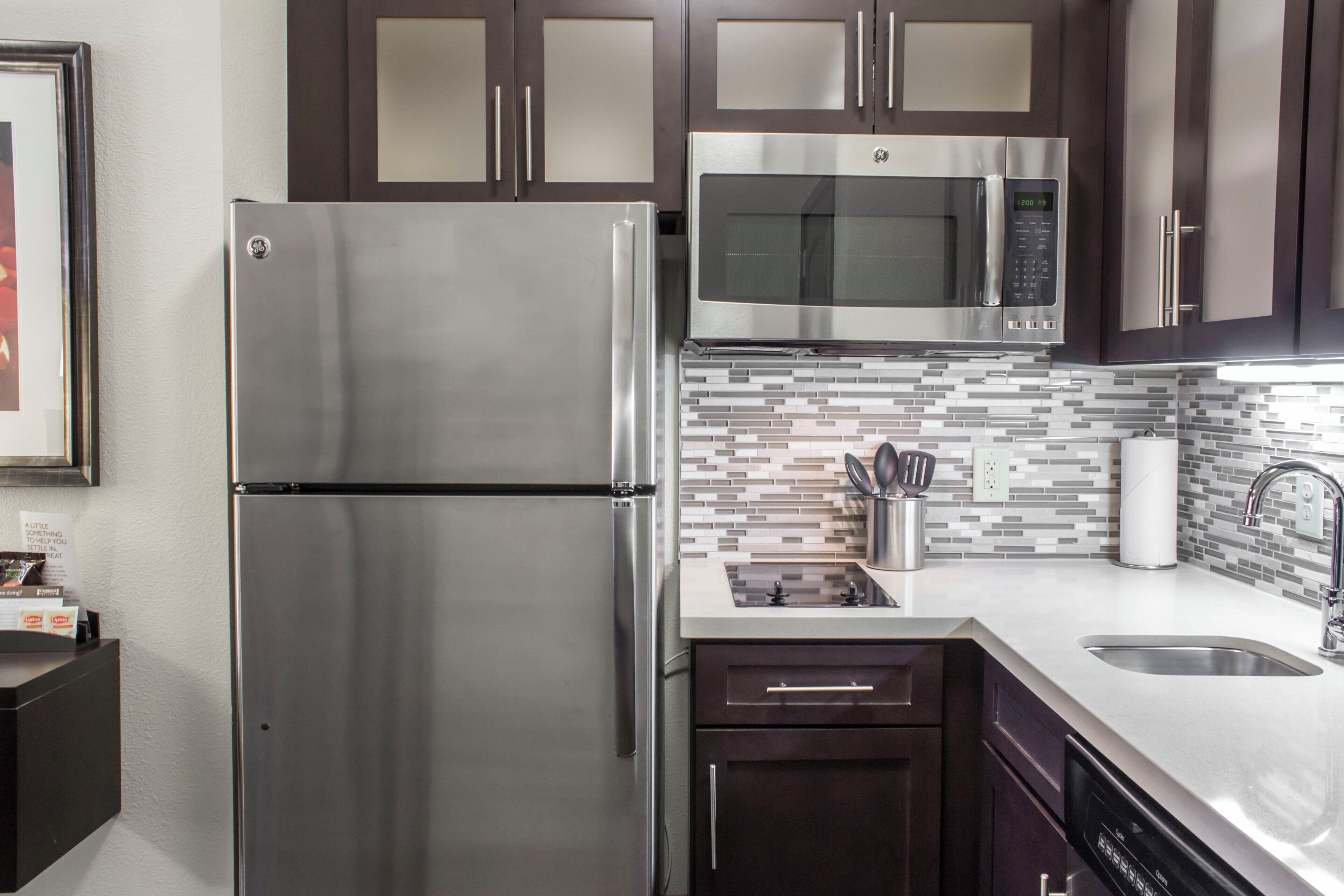 A modern kitchen with stainless steel appliances, a tiled backsplash, and dark cabinetry.