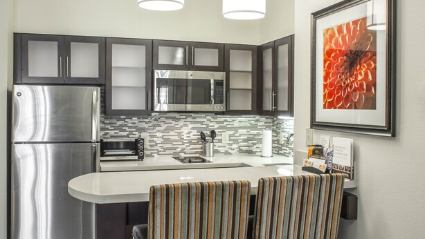 Una cocina moderna con electrodomésticos de acero inoxidable, salpicadero de azulejos y dos sillas a rayas junto a una pequeña isla.