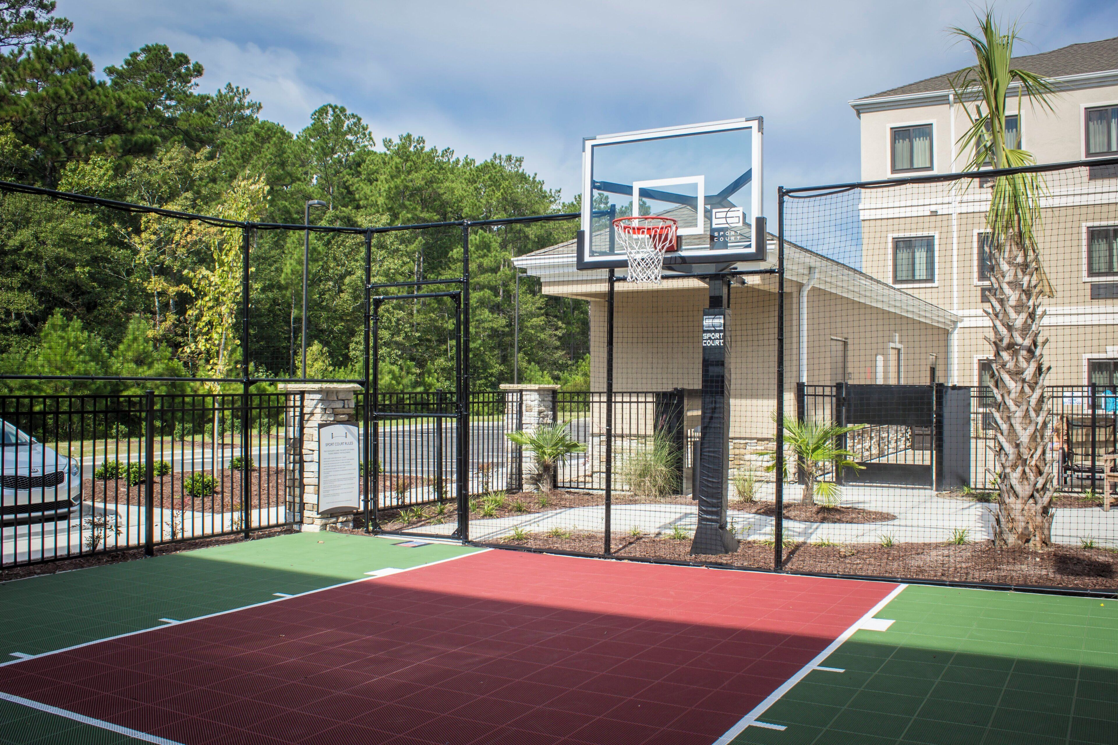 Een basketbalveld buiten, met een net, omgeven door een hek en bomen.