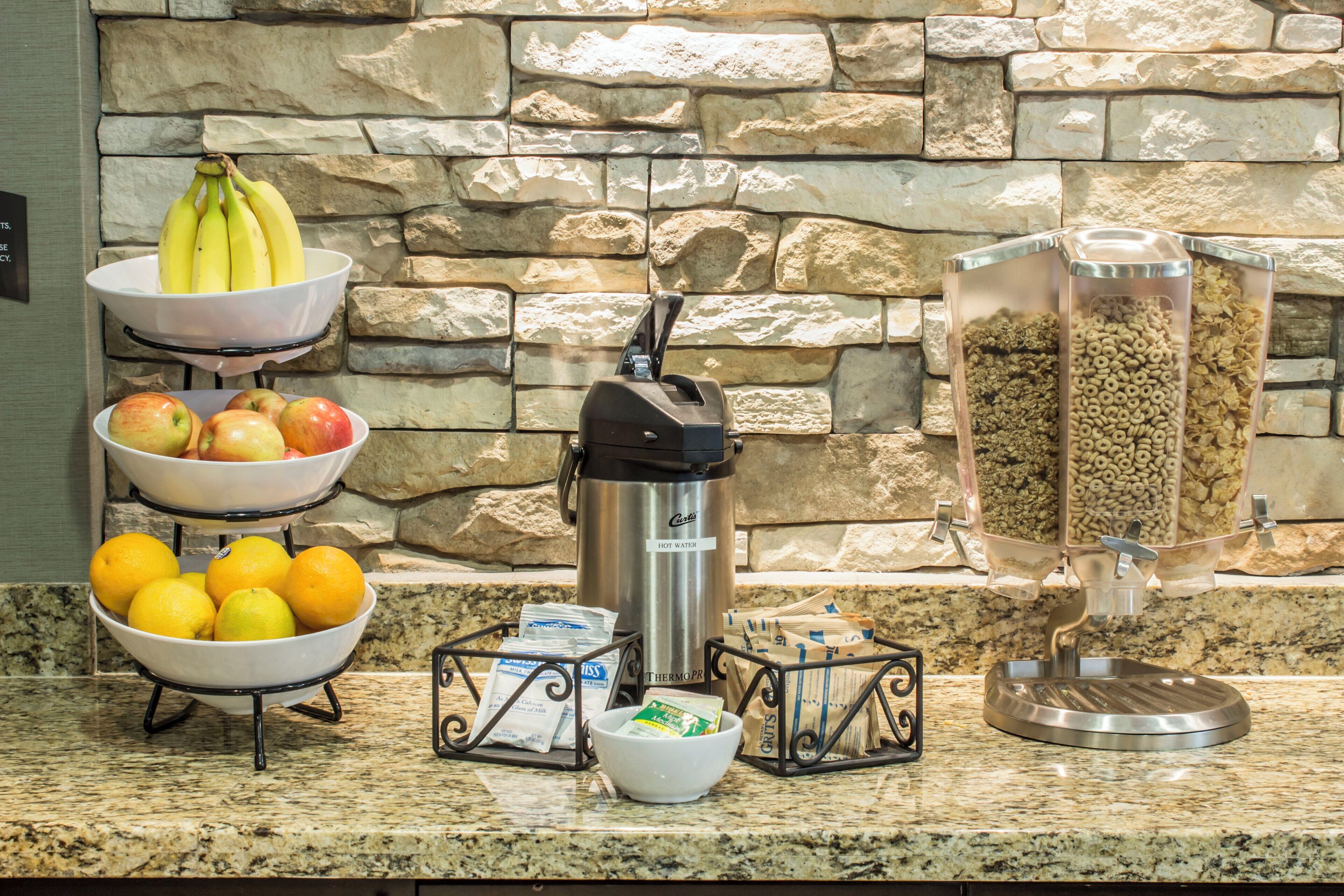 Una barra de desayuno con frutas, cereales y un dispensador de agua caliente.
