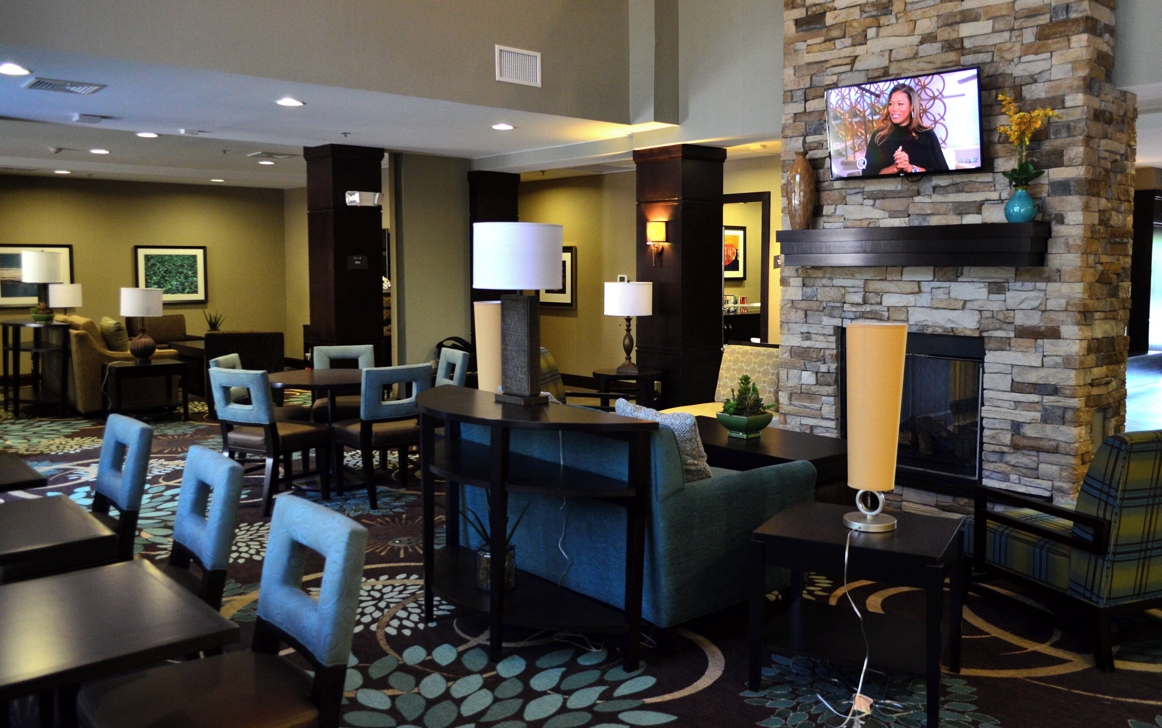 A hotel lobby with a television mounted on a stone wall, seating arrangements, and a fireplace.