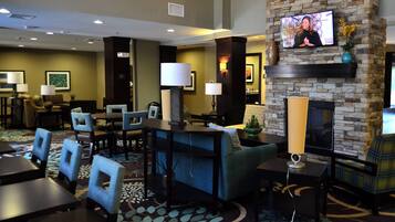 A hotel lobby with a television mounted on a stone wall, seating arrangements, and a fireplace.