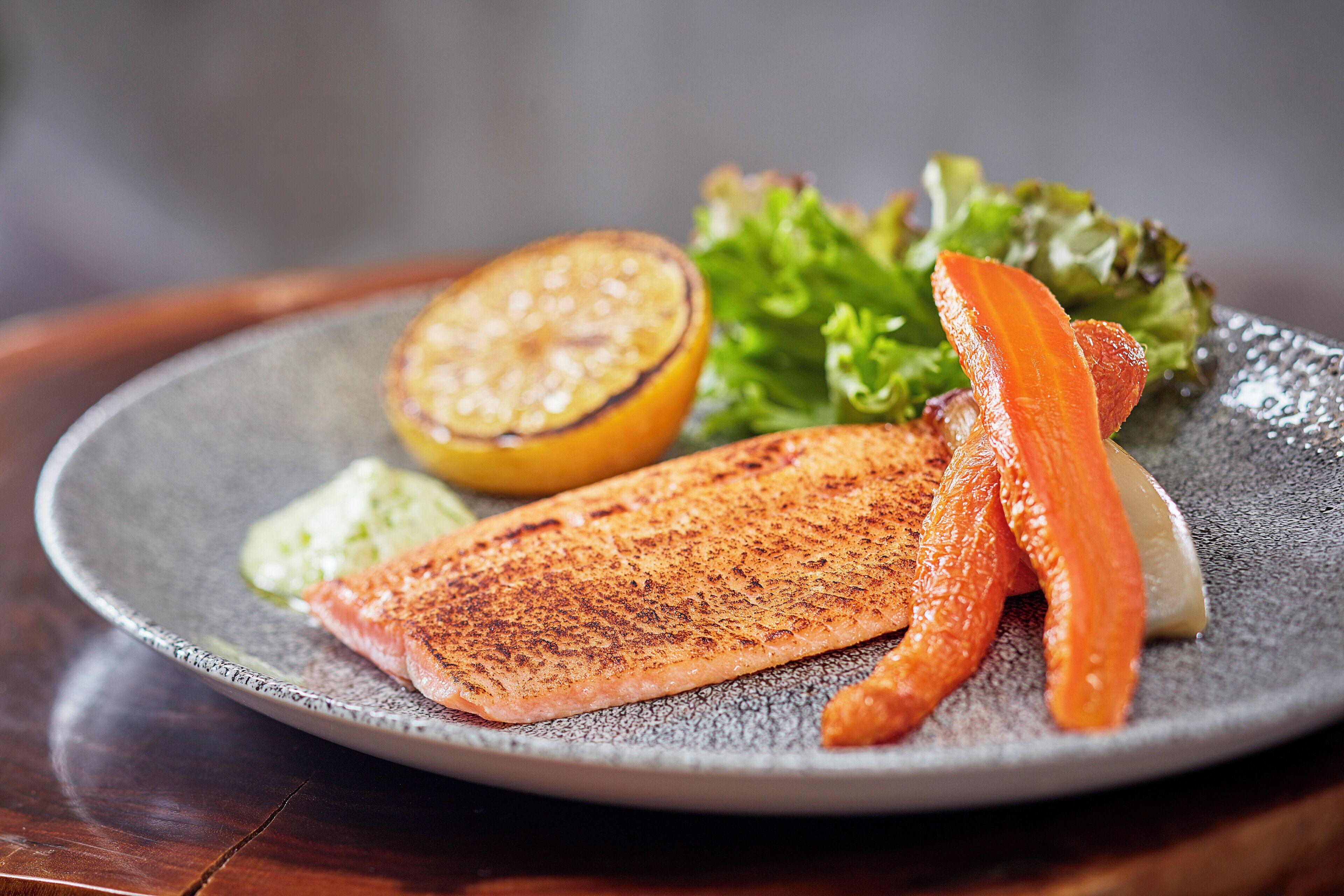 Une assiette contenant du saumon grillé, une moitié de citron et des rondelles de carottes.